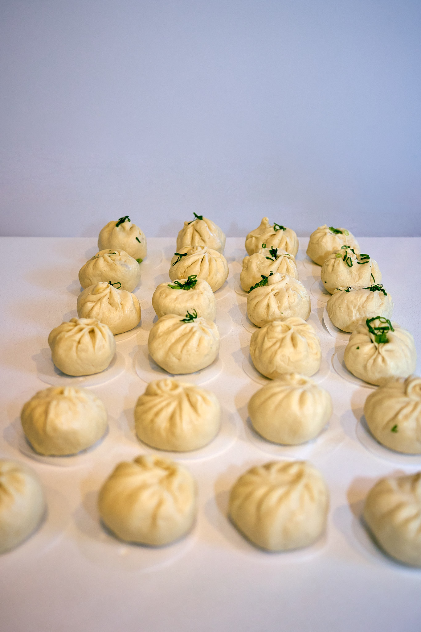 Rows of freshly steamed bao topped with spring onion, cooling on the bench